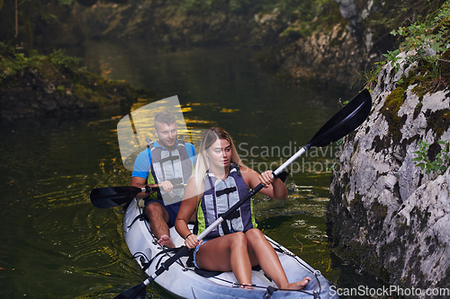 Image of A young couple enjoying an idyllic kayak ride in the middle of a beautiful river surrounded by forest greenery