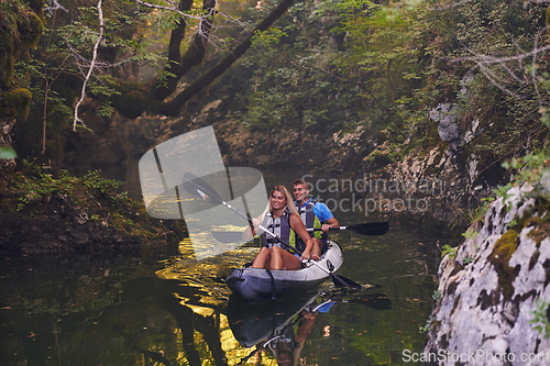 Image of A young couple enjoying an idyllic kayak ride in the middle of a beautiful river surrounded by forest greenery