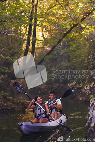 Image of A young couple enjoying an idyllic kayak ride in the middle of a beautiful river surrounded by forest greenery