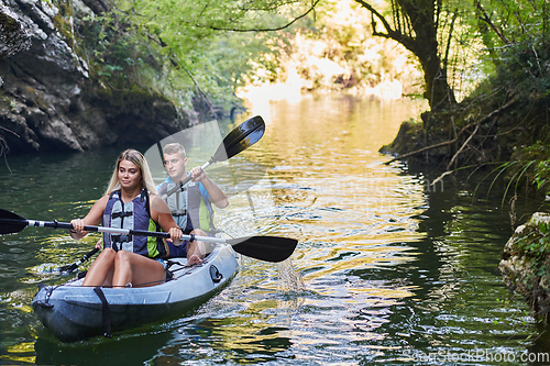 Image of A group of friends enjoying having fun and kayaking while exploring the calm river, surrounding forest and large natural river canyons