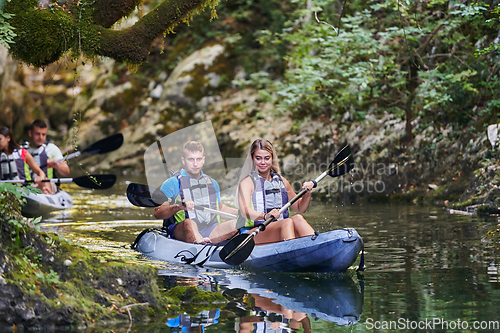 Image of A young couple enjoying an idyllic kayak ride in the middle of a beautiful river surrounded by forest greenery