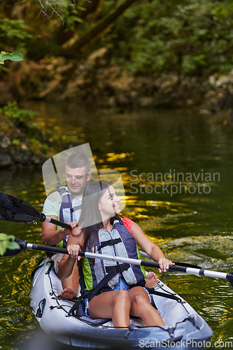 Image of A young couple enjoying an idyllic kayak ride in the middle of a beautiful river surrounded by forest greenery