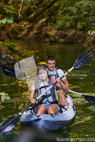 Image of A young couple enjoying an idyllic kayak ride in the middle of a beautiful river surrounded by forest greenery