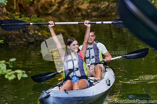 Image of A young couple enjoying an idyllic kayak ride in the middle of a beautiful river surrounded by forest greenery