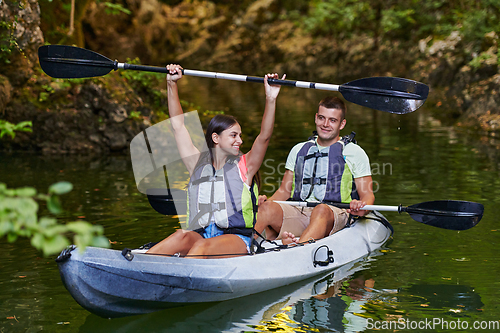 Image of A young couple enjoying an idyllic kayak ride in the middle of a beautiful river surrounded by forest greenery