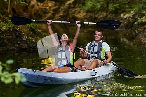 Image of A young couple enjoying an idyllic kayak ride in the middle of a beautiful river surrounded by forest greenery