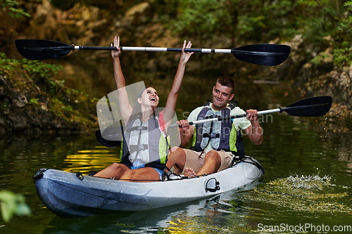 Image of A young couple enjoying an idyllic kayak ride in the middle of a beautiful river surrounded by forest greenery