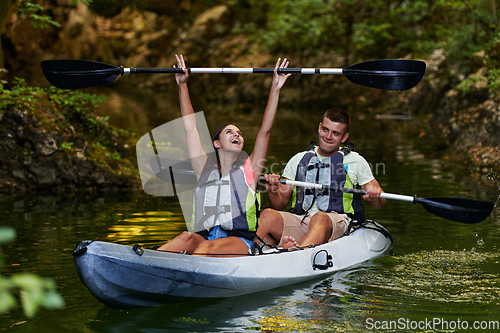 Image of A young couple enjoying an idyllic kayak ride in the middle of a beautiful river surrounded by forest greenery