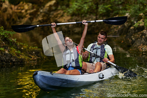 Image of A young couple enjoying an idyllic kayak ride in the middle of a beautiful river surrounded by forest greenery