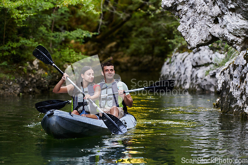 Image of A young couple enjoying an idyllic kayak ride in the middle of a beautiful river surrounded by forest greenery