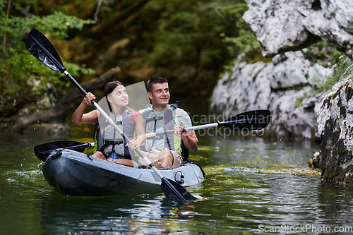 Image of A young couple enjoying an idyllic kayak ride in the middle of a beautiful river surrounded by forest greenery