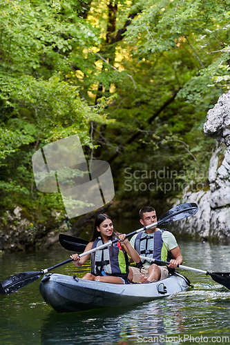 Image of A young couple enjoying an idyllic kayak ride in the middle of a beautiful river surrounded by forest greenery