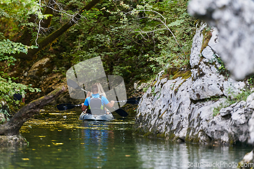 Image of A young couple enjoying an idyllic kayak ride in the middle of a beautiful river surrounded by forest greenery