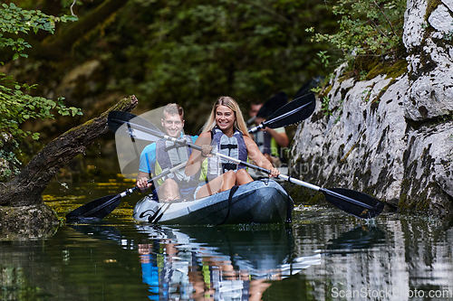 Image of A group of friends enjoying having fun and kayaking while exploring the calm river, surrounding forest and large natural river canyons