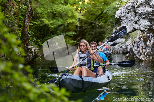 Image of A group of friends enjoying having fun and kayaking while exploring the calm river, surrounding forest and large natural river canyons