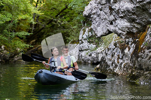 Image of A young couple enjoying an idyllic kayak ride in the middle of a beautiful river surrounded by forest greenery