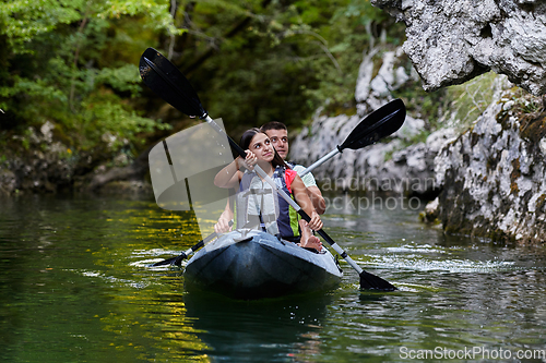 Image of A young couple enjoying an idyllic kayak ride in the middle of a beautiful river surrounded by forest greenery