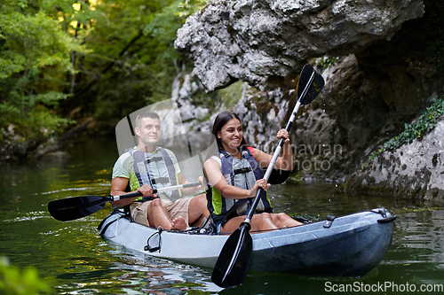 Image of A young couple enjoying an idyllic kayak ride in the middle of a beautiful river surrounded by forest greenery