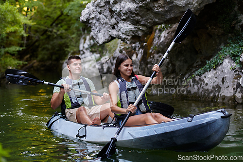 Image of A young couple enjoying an idyllic kayak ride in the middle of a beautiful river surrounded by forest greenery