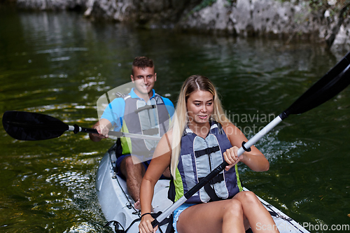 Image of A young couple enjoying an idyllic kayak ride in the middle of a beautiful river surrounded by forest greenery