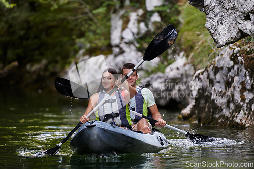 Image of A young couple enjoying an idyllic kayak ride in the middle of a beautiful river surrounded by forest greenery