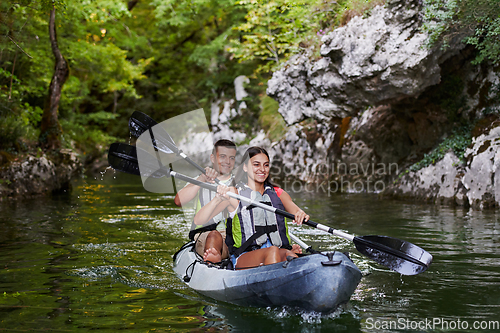 Image of A young couple enjoying an idyllic kayak ride in the middle of a beautiful river surrounded by forest greenery