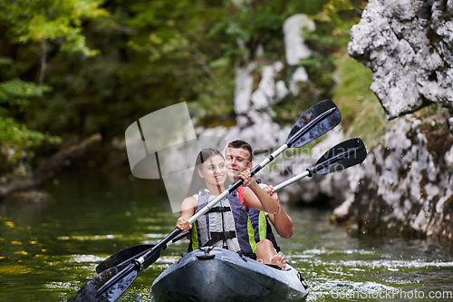 Image of A young couple enjoying an idyllic kayak ride in the middle of a beautiful river surrounded by forest greenery