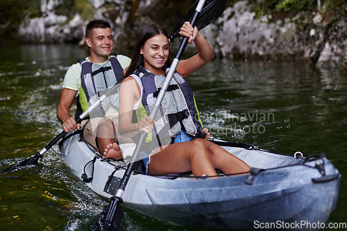 Image of A young couple enjoying an idyllic kayak ride in the middle of a beautiful river surrounded by forest greenery