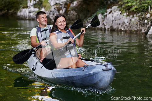 Image of A young couple enjoying an idyllic kayak ride in the middle of a beautiful river surrounded by forest greenery