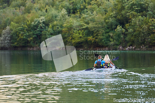 Image of A young couple enjoying an idyllic kayak ride in the middle of a beautiful river surrounded by forest greenery