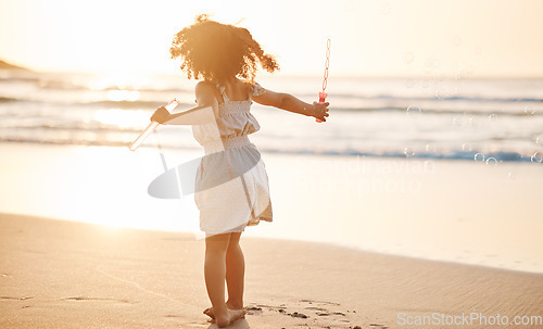 Image of Girl child, bubbles and back by beach in sunset, playing and freedom by waves, games and ocean vacation. Young female kid, plastic toys and soap with water in summer sunshine by sea for holiday