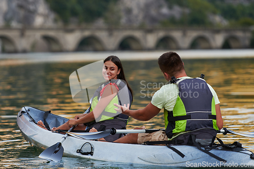 Image of A young couple enjoying an idyllic kayak ride in the middle of a beautiful river surrounded by forest greenery