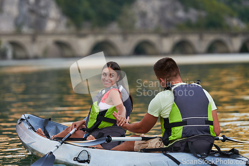 Image of A young couple enjoying an idyllic kayak ride in the middle of a beautiful river surrounded by forest greenery