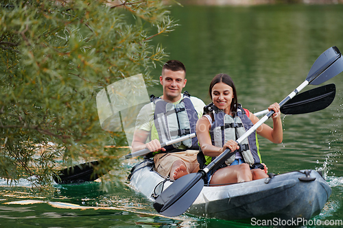 Image of A young couple enjoying an idyllic kayak ride in the middle of a beautiful river surrounded by forest greenery