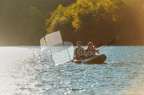 Image of A young couple enjoying an idyllic kayak ride in the middle of a beautiful river surrounded by forest greenery in sunset time