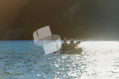 Image of A young couple enjoying an idyllic kayak ride in the middle of a beautiful river surrounded by forest greenery in sunset time