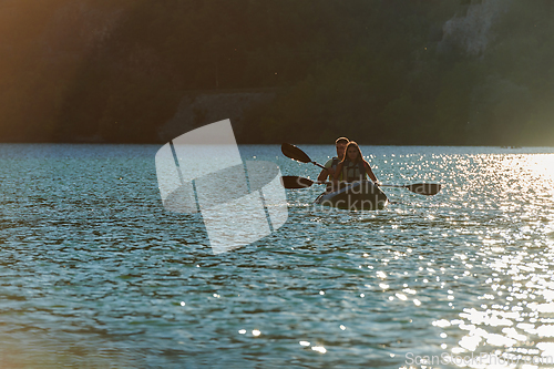 Image of A young couple enjoying an idyllic kayak ride in the middle of a beautiful river surrounded by forest greenery in sunset time