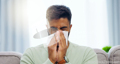 Image of Tissue, sneeze and Indian man blowing nose on a home living room sofa feeling sick and tired. Allergy problem, virus and toilet paper of a person on a house lounge couch with sinus infection and flu