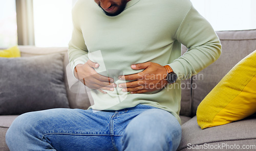 Image of Man on a sofa with stomach pain, sickness or cramps while relaxing in the living room at his home. Medical emergency, illness and male with diarrhea, indigestion or food poisoning ache at his house.