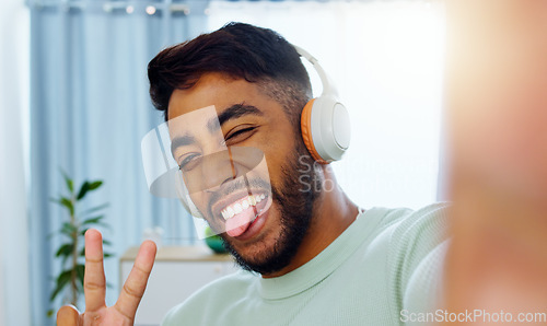 Image of Selfie, man and smiling tongue out emoji headphones for music playlist streaming and cheerful mood in home. Wellness peace sign, audio and happy male ready to dance photograph with smile.