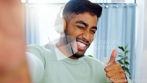 Image of Selfie, man and smiling thumbs up emoji headphones for music playlist streaming and cheerful mood in home. Wellness peace sign, audio and happy male ready to dance photograph with smile wink