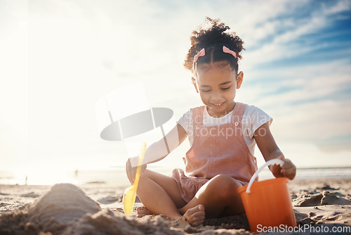 Image of Sand, castle and girl kid at beach for fun games, freedom and summer holiday with mockup sky. Happy child, bucket and building with play toys at sea for development, vacation and relax in sunshine