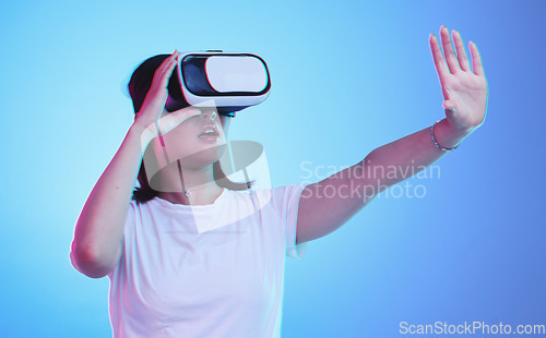 Image of Metaverse, headset and a woman on a blue background, touching for experience and VR gaming. Virtual reality, digital and a girl with glasses for a 3d online game or entertainment on a studio backdrop