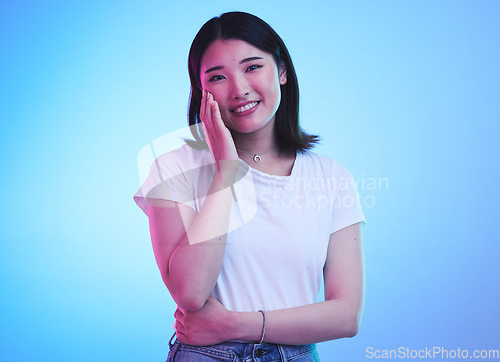 Image of Face, smile and Asian woman with beauty or dream with hope or happiness isolated in a studio blue background. Cute, shy and happy young female person with skincare or soft skin and with a memory