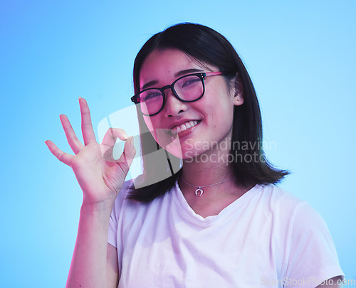 Image of Woman, okay hands or sign for learning success, certified and excellence in tshirt and a blue, studio background. Happy young, asian person in glasses, portrait and yes or support emoji for education