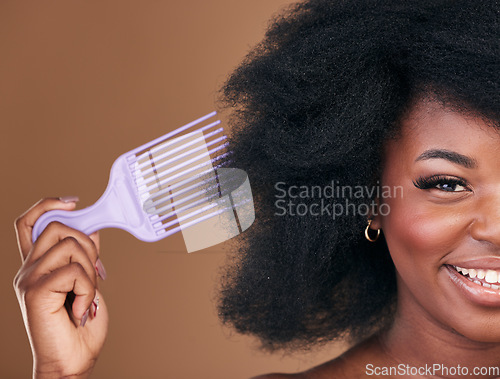 Image of Portrait, hair and comb with a natural black woman in studio on brown background for cosmetics. Face, smile and haircare with a happy young model brushing her afro after for shampoo treatment