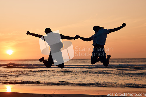 Image of Beach sunset, shadow silhouette and couple jump, holding hands and having fun, bonding and enjoy nature freedom. Sky, tropical ocean sea and excited people celebrate outdoor travel on spring vacation