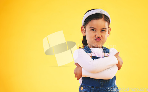 Image of Arms crossed, portrait and angry girl child in studio with bad, attitude or behavior problem on yellow background. Frown, face and asian kid with body language for no, frustrated or tantrum emoji