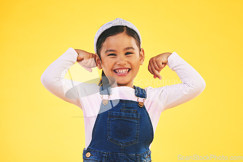 Image of Smile, portrait and girl child with arm flex in studio for confidence, strong and power on yellow background. Happy, face and excited kid with bicep strength, pose or empower, positive or growth sign