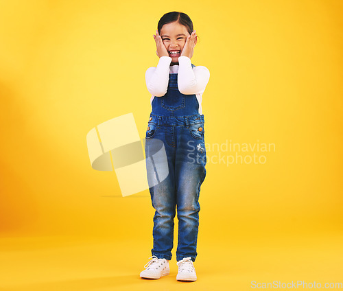 Image of Excited, happy and hands on face of girl child in studio with news, sale or fashion giveaway on yellow background. Wow, emoji and kid winner with celebration gesture for coming soon surprise prize